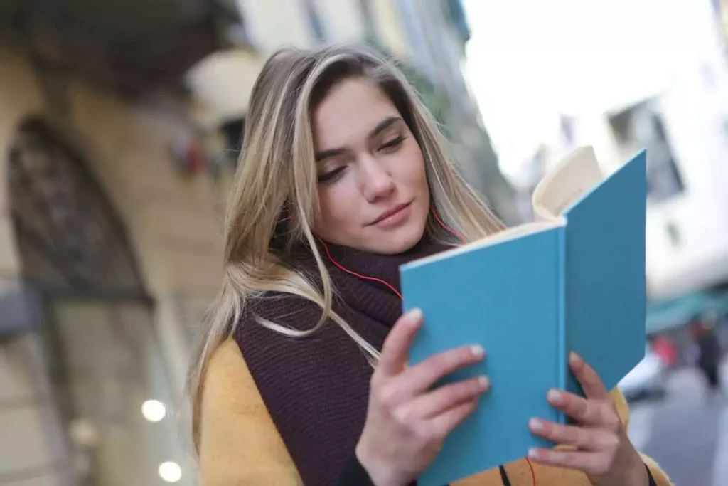 Woman holding the book and reading while walking outdoors