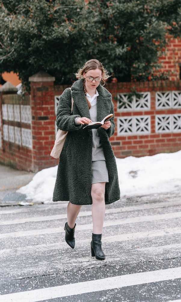 Woman reading a book while crossing a road