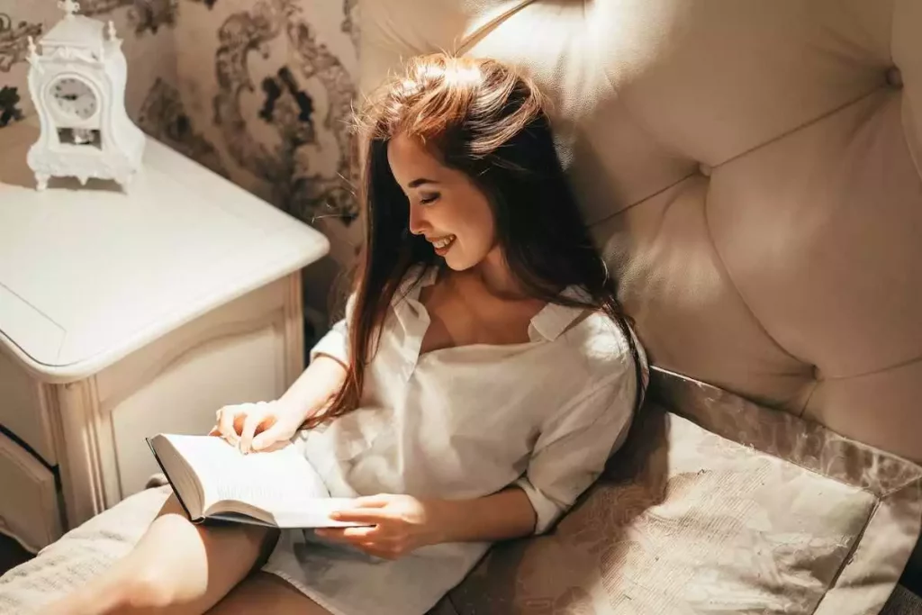 woman smiling and reading a book while sitting on the bed