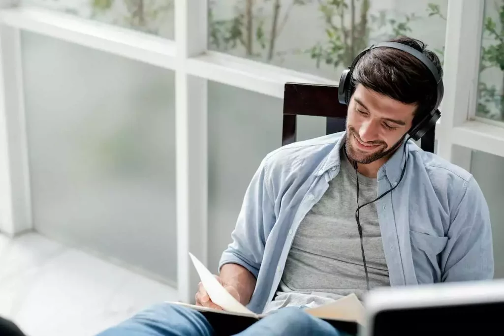 caucasian man reading book and listening to music with headphones