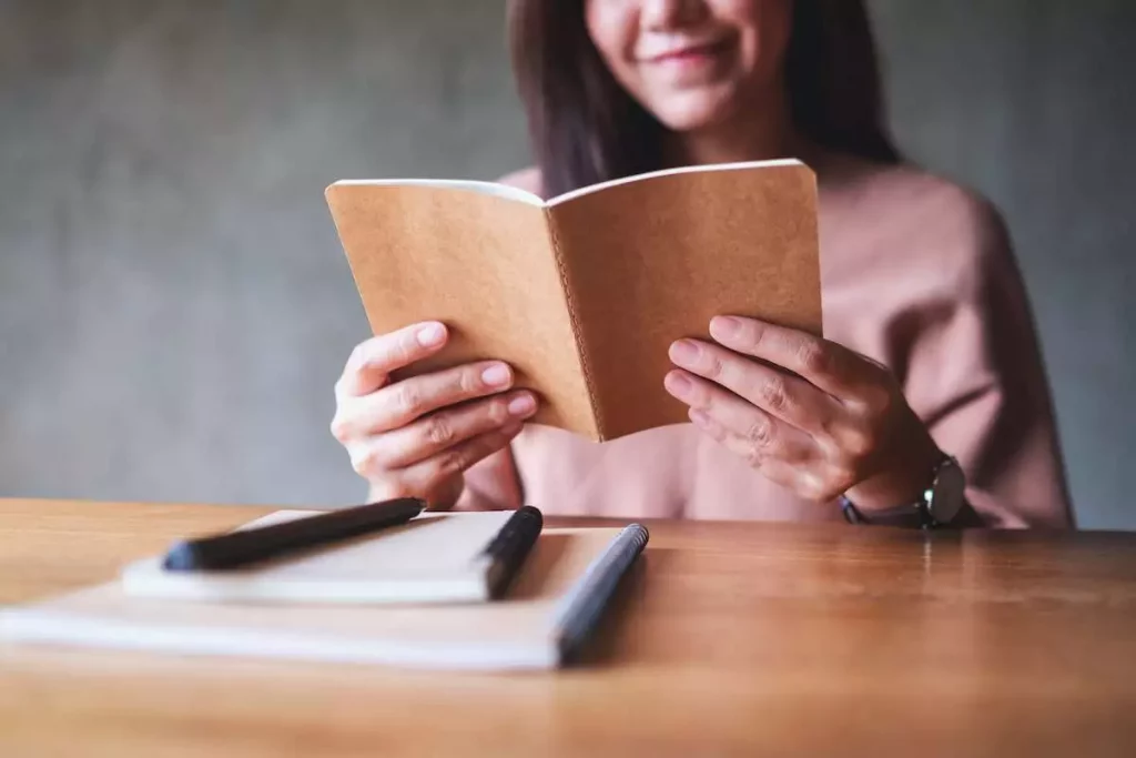 closeup image of a young woman writer reading a book to improve writing skills