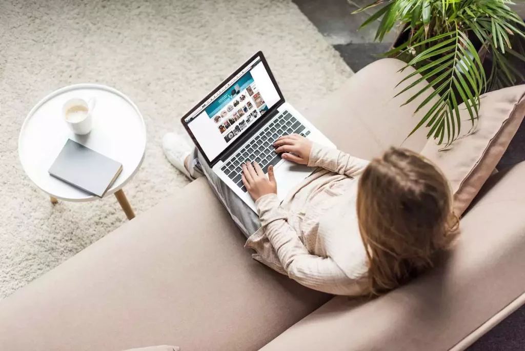 woman sitting on a couch with a laptop trying to figure out how to find the Kindle email address on Amazon