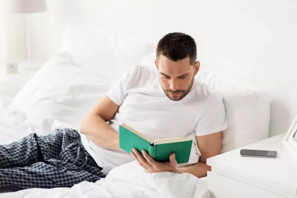 Man reading a book in bed at home