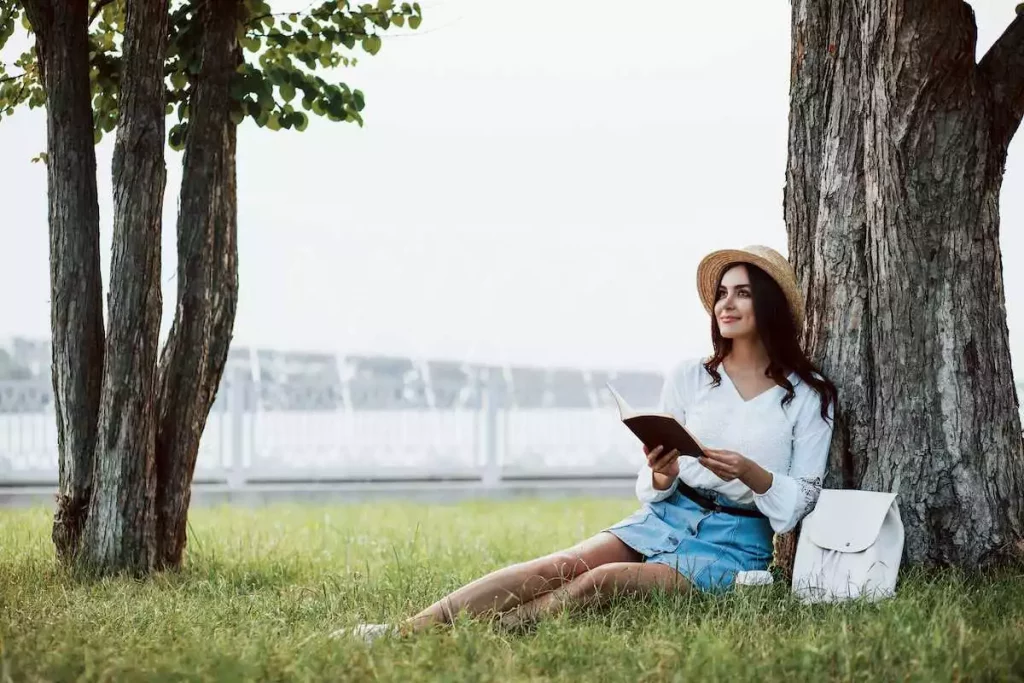 young beautiful woman reading a book in the park while imagining