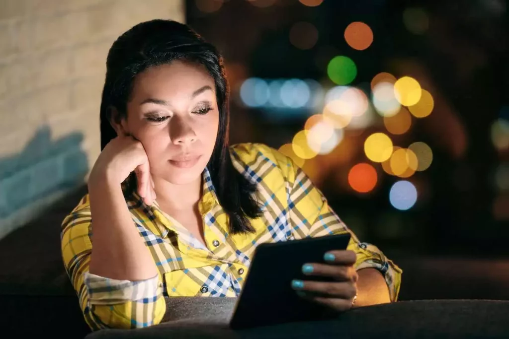 woman reading on a Kindle ebook reader at night on a sofa